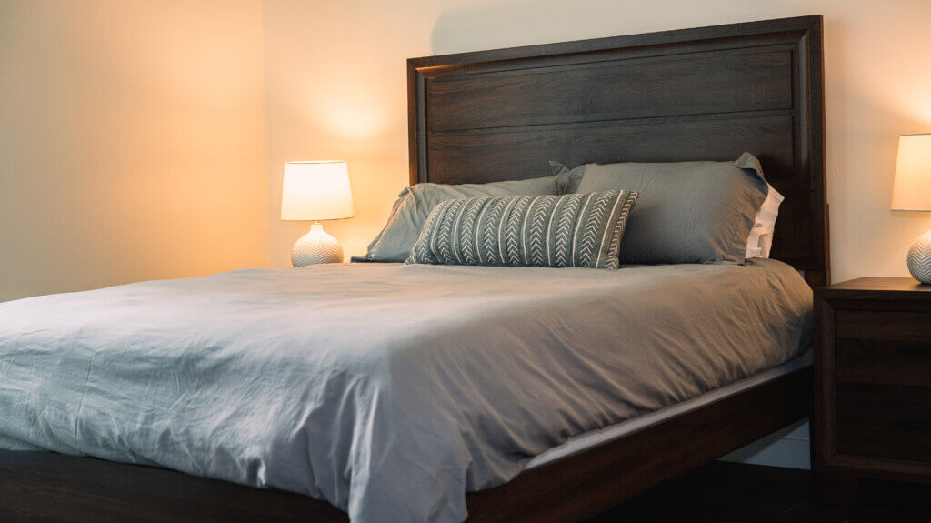 A well-made queen-sized bed with nightstands and lamps one either side in a fully furnished apartment