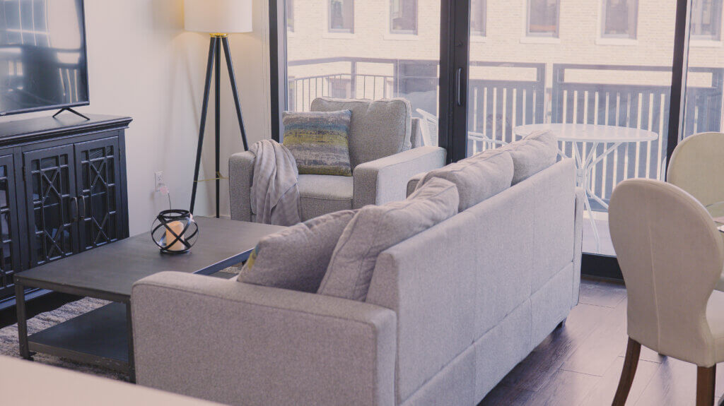 A grey couch in the center of a well decorated living room in a fully furnished apartment